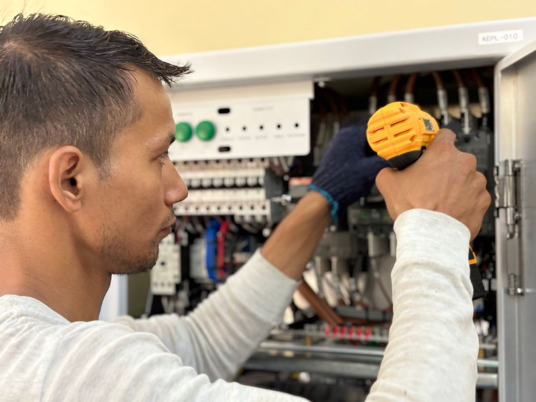 Técnico de campo trabalhando em um painel elétrico durante uma ordem de serviço, usando parafusadeira sobre disjuntores e contatores